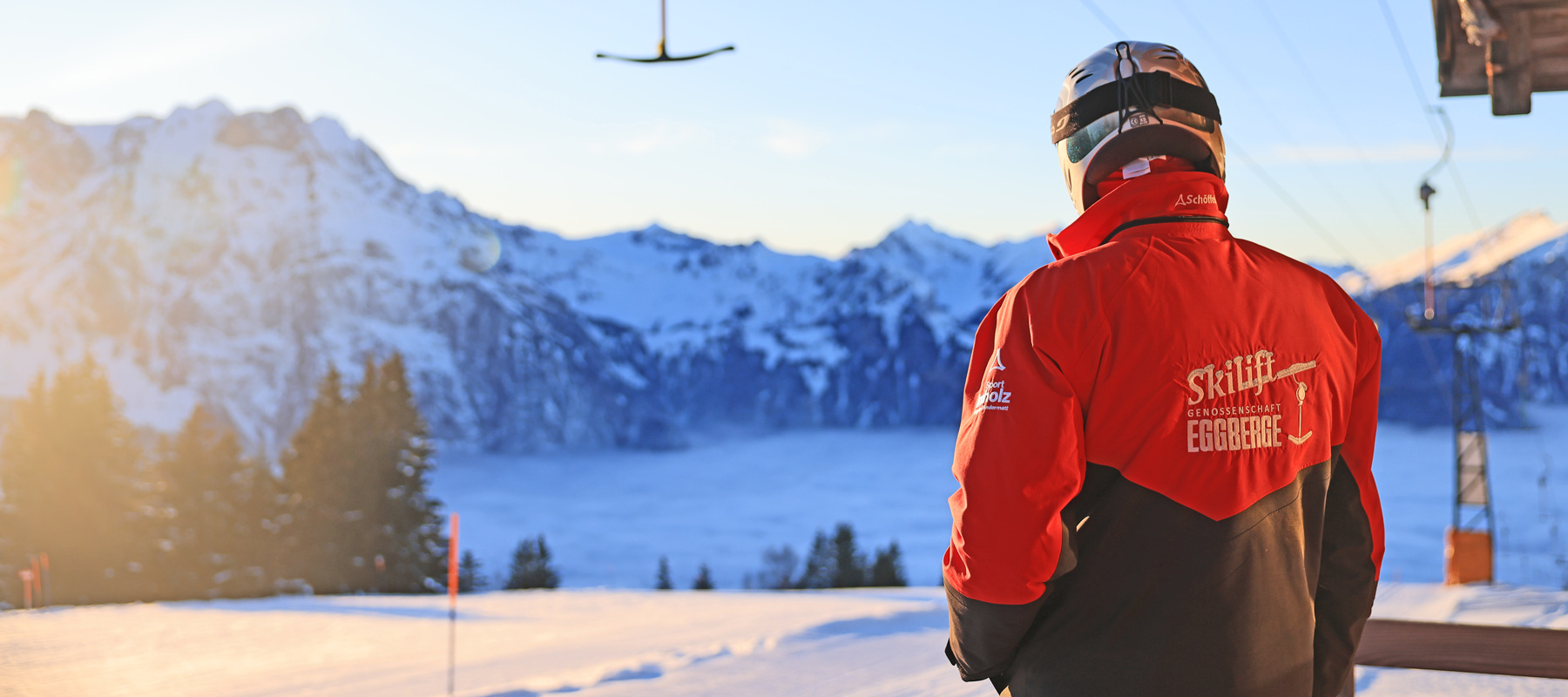 Winter sports enthusiasts enjoy the snow at Eggberge ski resort in Altdorf, Central Switzerland. Skiers and a snowboarder carve down the slopes, with a ski lift visible in the background.