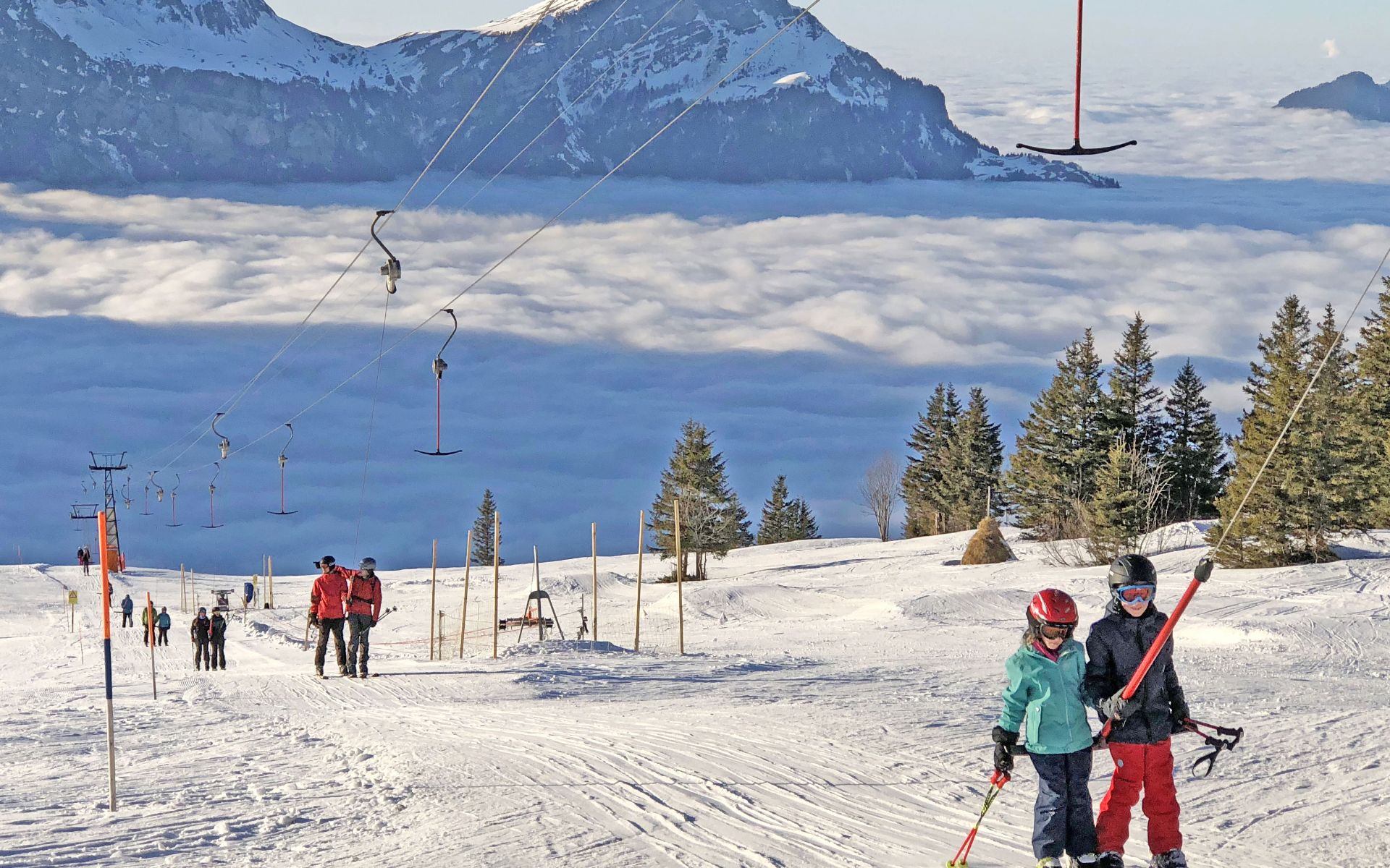 Winter sports scene at Eggberge in Uri, Switzerland, featuring a bustling ski resort with a ski lift, a family enjoying skiing on the snow-covered slopes in the picturesque Reuss Valley.