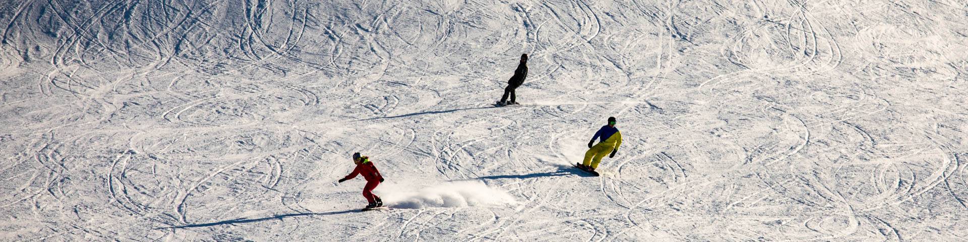 A winter sports scene at Gesundaberget in Sollerön Sweden featuring a skier and a snowboarder gliding down the snowy slopes. The scene is complemented by a picturesque challet in the background and a ski lift nearby.
