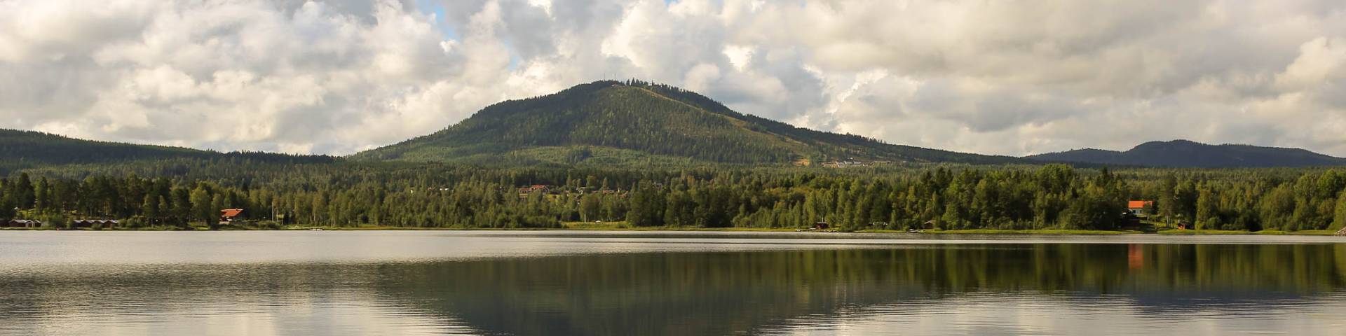 View of serene lake at the base of Gesundaberget mountain in Sollerön, Sweden, with a quaint chalet and lodge nestled nearby, hinting at its ski resort attributes.