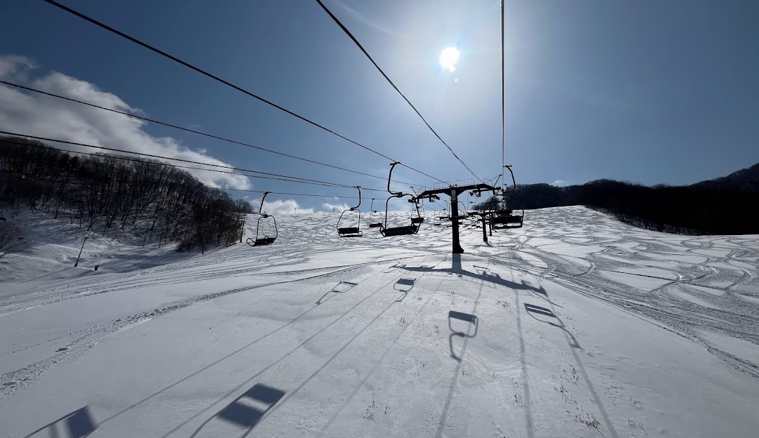 View of Okutone Snow Park in Japan featuring a ski lift and skiers enjoying the winter sports scene at a resort, with a challet visible in the background amidst stunning winter scenery.