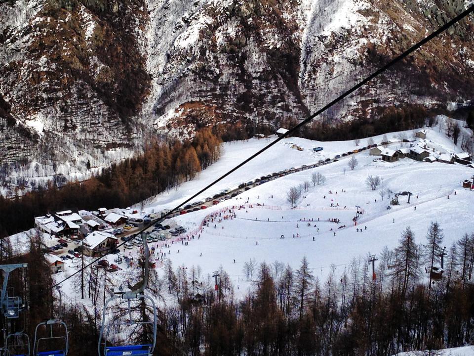 Winter vista at Pian Benot Sciovie Usseglio ski resort in Turin, Italy, featuring a bustling ski scene, a looming ski lift, and a charming chalet nestled in the snow-covered landscape.