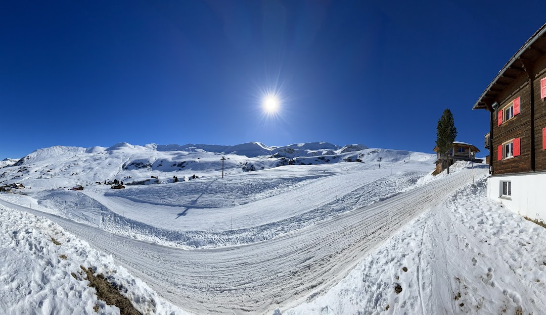 A charming chalet situated in Fideriser Heuberge, Eastern Switzerland, amid a bustling winter sports scene. A ski resort and sports center complement the serene winter scenery.