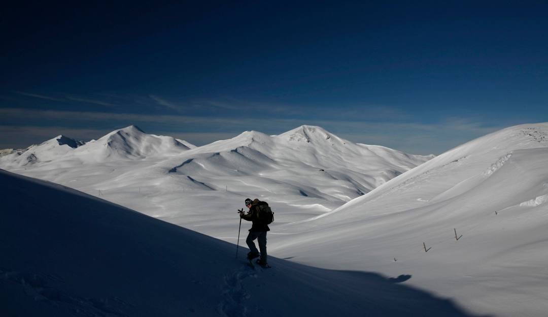 A skier glides down the slopes at the winter sports resort of Fideriser Heuberge in Graubünden, Eastern Switzerland. A quaint chalet peeks through the pristine snow, enhancing the stunning winter scenery.