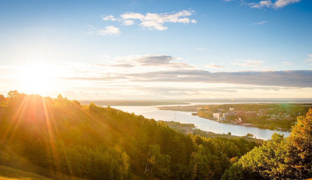 Sunny day at Mont Ripley in Hancock, Michigan, showcasing a chalet by a tranquil lake with mountains in the background and elements of a ski resort.