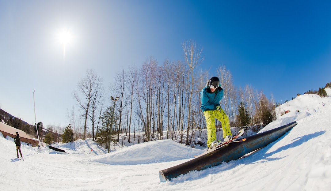 A skier and snowboarder descending a hill at Mont Ripley in Hancock, Michigan, with a ski lift and the ski resort appearing amidst a lively winter sports scene.