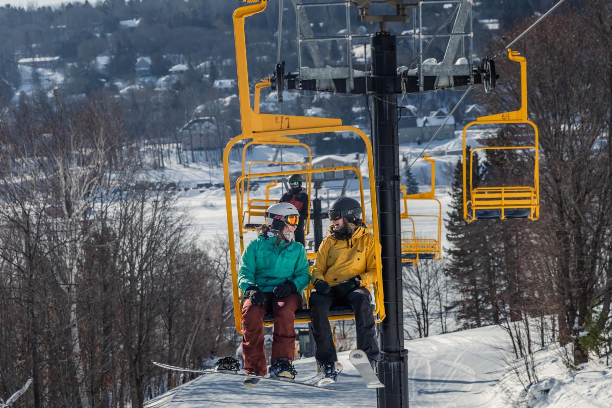 Mont Ripley in USA - two people sitting on a ski lift in the snow.