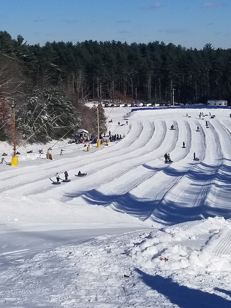 Winter sports scene at Nashoba Valley Ski Area in Westford, Massachusetts, featuring a skier heading downhill and a snowmobile in the distance.
