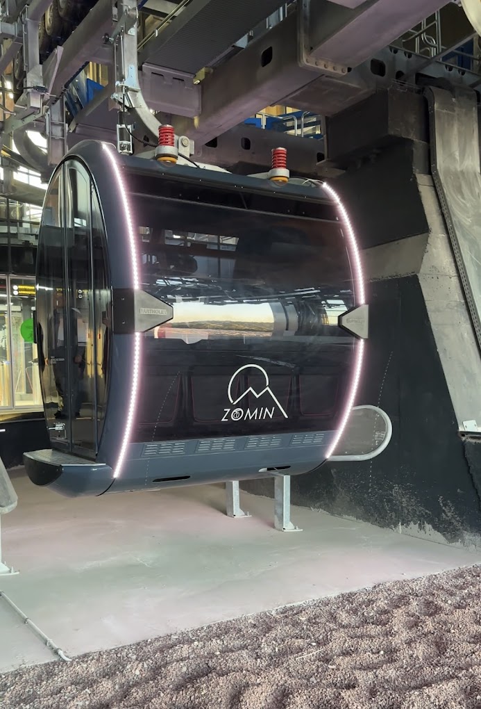 A picturesque view of the Zomin Ropeway in Uzbekistan. A challet and a snowmobile are in focus while a ski lift is faintly visible. Groomer and mountain barely discernible in the backdrop.