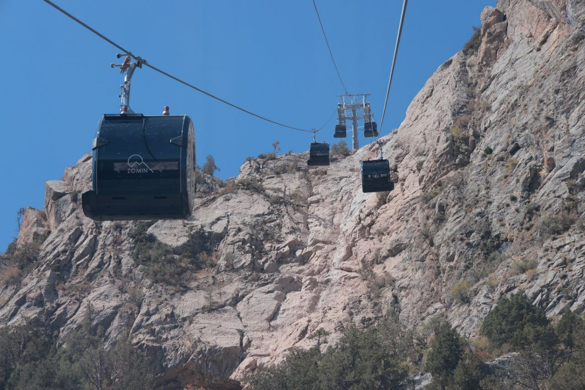 View of Zomin Ropeway in Uzbekistan featuring a ski lift ascending a snow-covered mountain, leading to a chalet nestled amidst a scenic winter landscape, indicative of a bustling ski resort.