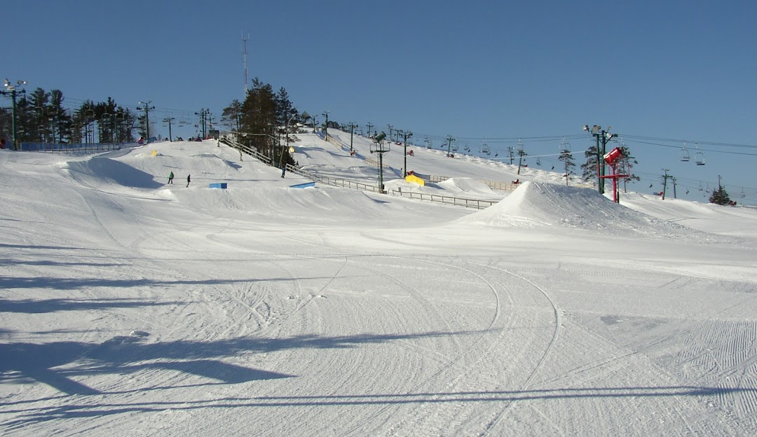 A skier gliding on the snowy landscape of Pine Knob ski resort in Village of Clarkston, Michigan, with a rustic chalet in the backdrop.