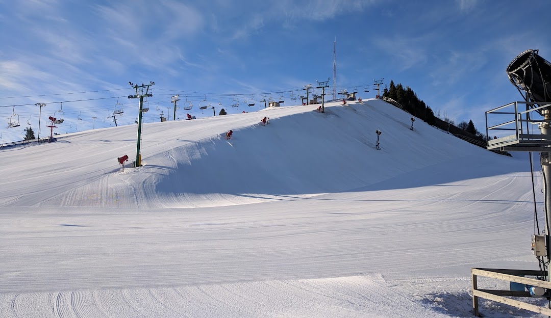 A ski resort in Pine Knob Clarkston Michigan with a busy winter sports scene. Various enthusiasts dot the snowy landscape accompanied by features such as a chalet and skier.