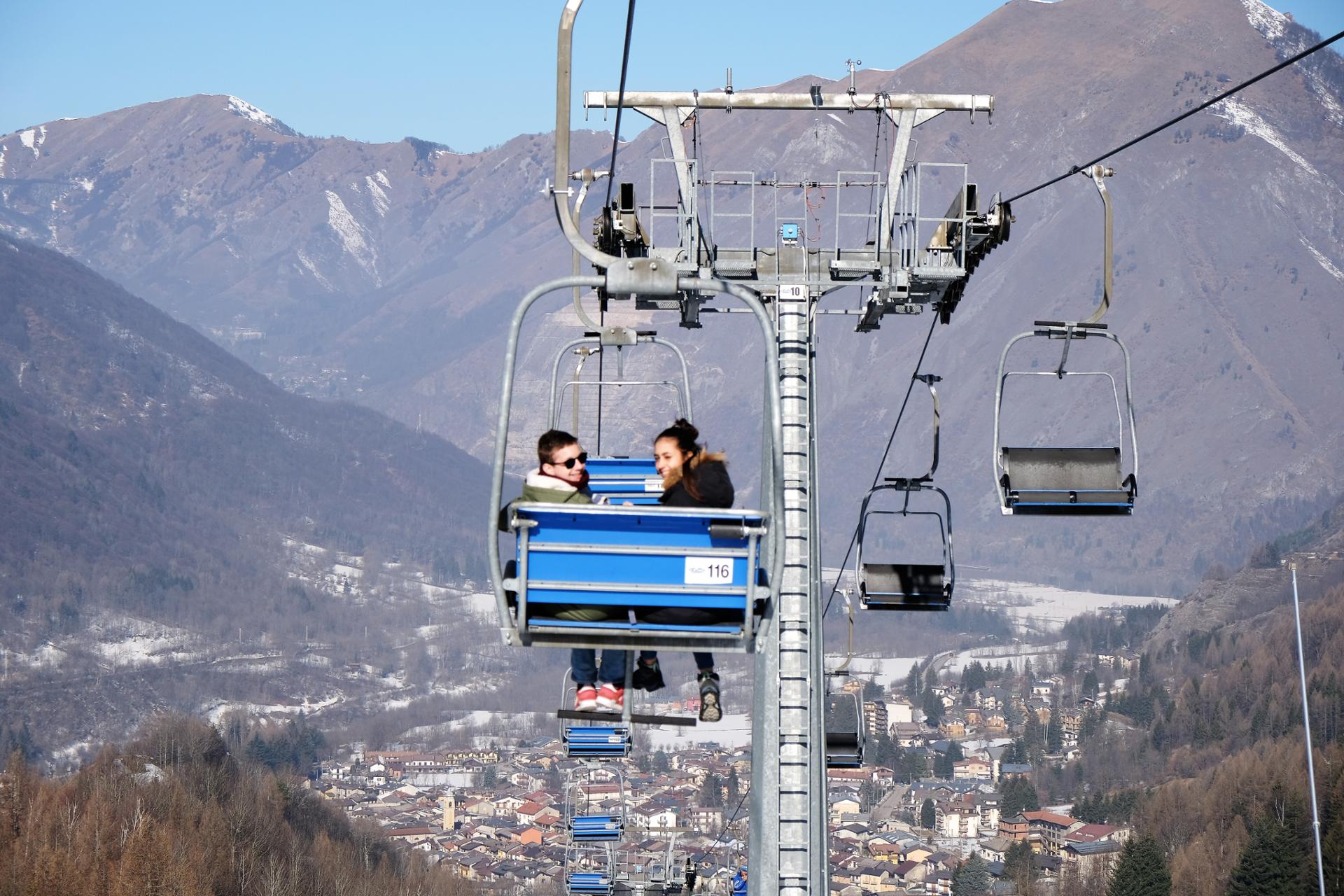 A scenic view of Entracque ski resort in Italy featuring a ski lift traversing the snow-covered slopes. The landscape is dotted with a charming chalet embodying a lively winter sports scene.
