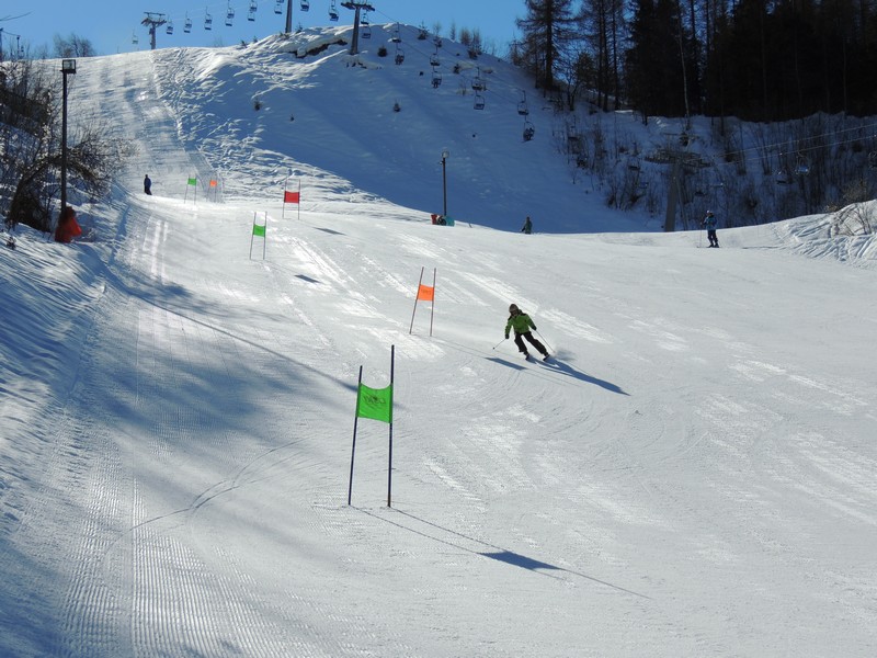 Skier enjoying a winter sports scene in Entracque, Piedmont, amidst a popular ski resort. Evidence of a bustling winter sports center can be seen in the background.