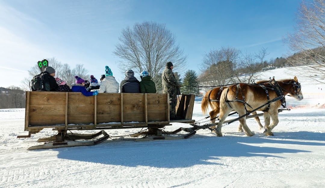 Winter sports scene in Quechee, Vermont featuring skiers in action amid a picturesque snowy landscape, with a chalet and a winter sports centre in view.