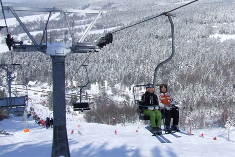 A skier enjoys a powdery day on the slopes at the Deštné ski resort in Czech Republic ascending the mountain via ski lift with a charming challet in the backdrop.
