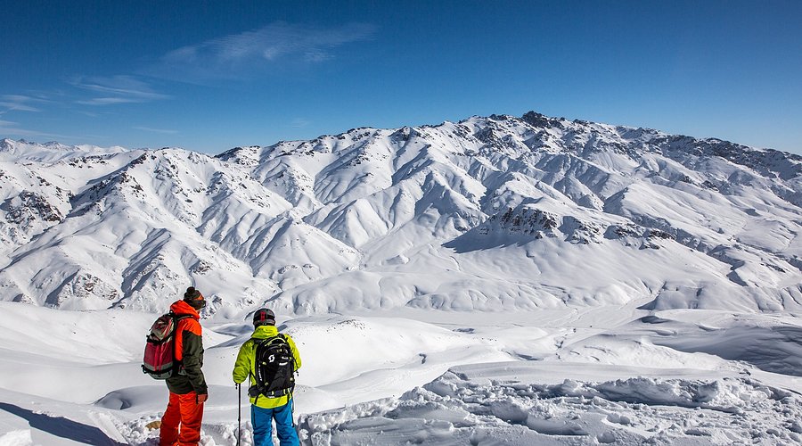 A lively winter sports scene at Too Ashuu Ski base in Kyrgyzstan featuring a skier and a group of people, against the backdrop of a ski resort and a charming chalet.