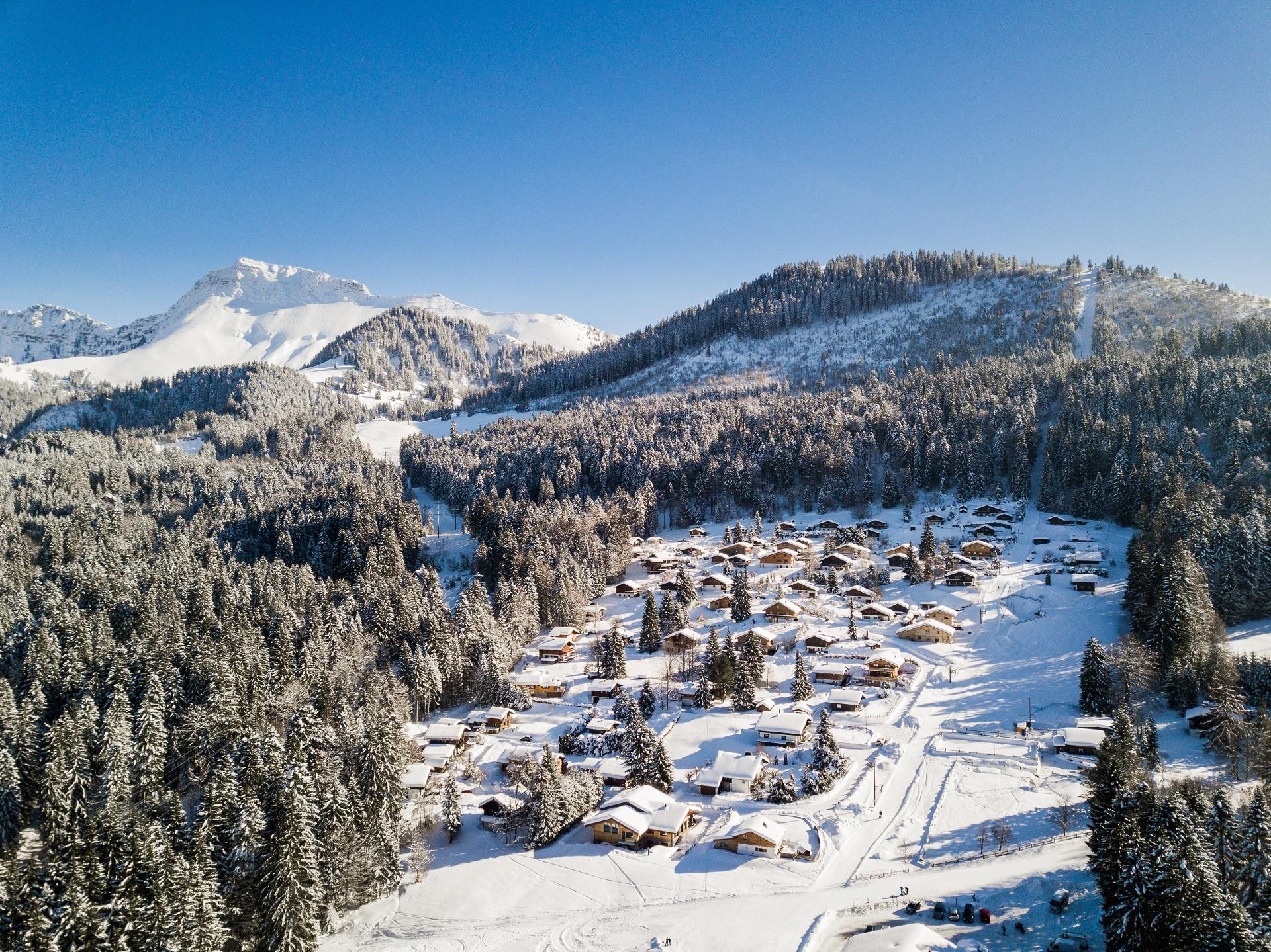 View of Les Paccots ski resort in Switzerland, with winter sports enthusiasts in action. Prominent are a cozy chalet and stunning winter scenery with white snowy landscapes.