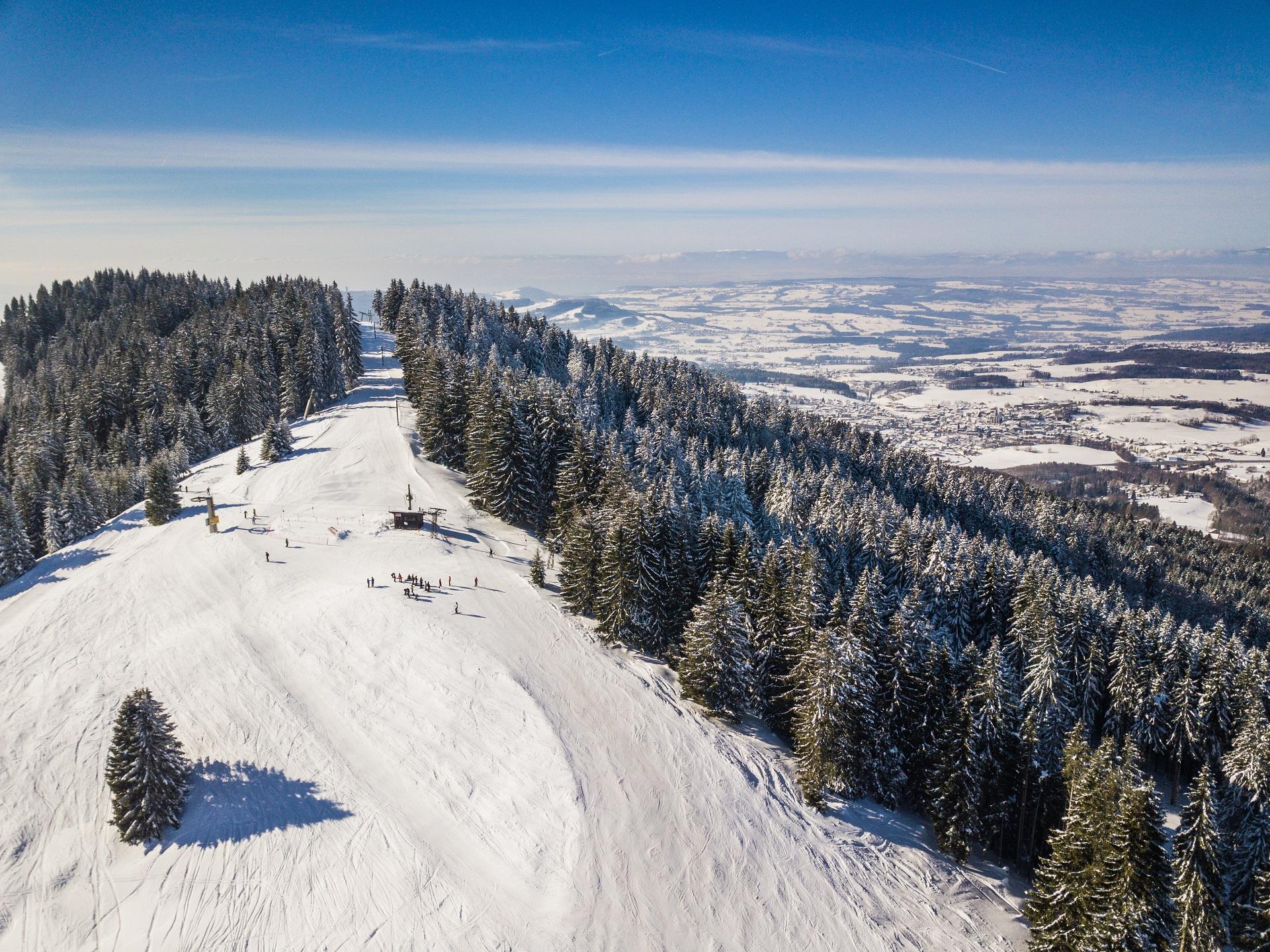 Winter scene at Les Paccots ski resort in Fribourg, Switzerland, featuring skiers enjoying the snowy slopes, with a ski lift in the background.