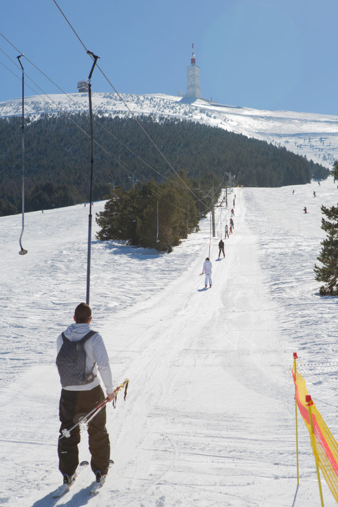 Winter sports scene at Mont Serein ski resort in Beaumont-du-Ventoux, France, featuring a skier, chalet, and winter sports centre.