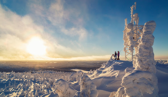 Winter sports scene in Iso-Syöte, Northern Finland featuring a family skiing amidst stunning winter scenery with snow-covered trees and a distant mountain view.