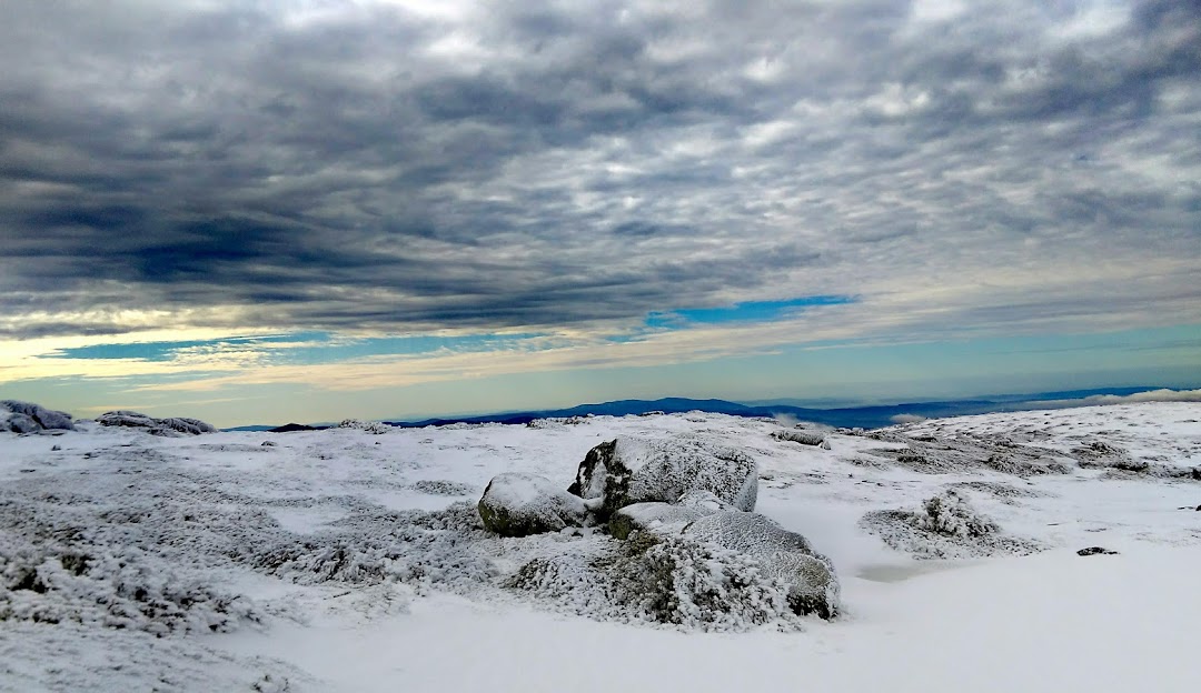 View of the picturesque Serra da Estrela in Covilhã, Portugal; a captivating scene of a snow-covered mountain peak against a clear winter sky, with traces of winter sport activities evident.