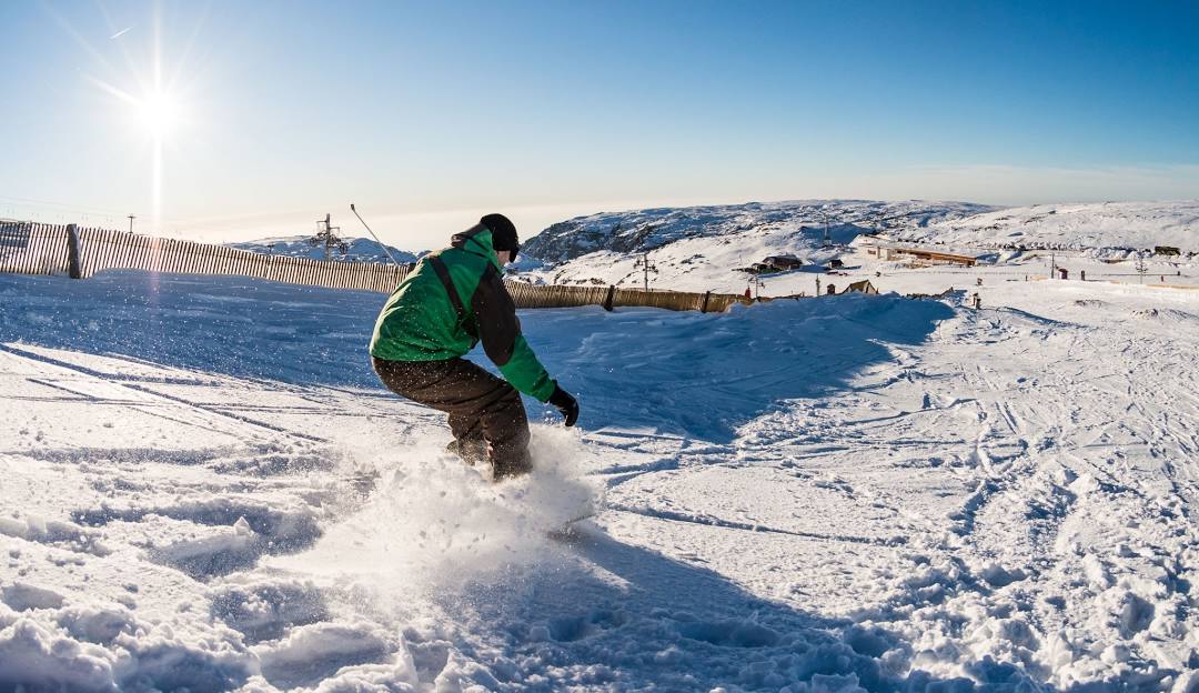 A snowboarder sliding down the snowy slopes of Serra da Estrela in Covilhã, Portugal, showcasing a picturesque winter scene.