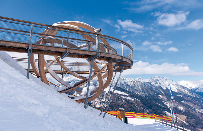 A vibrant view of the Elfer-Neustift ski resort in Tyrol, Austria, featuring a ski lift, a chalet, and people participating in winter sports.