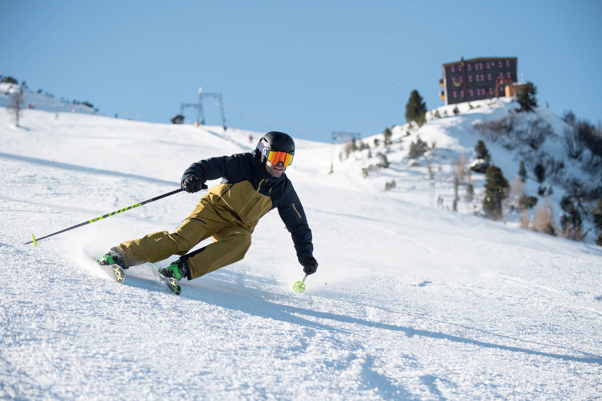 A skier and a snowboarder enjoying a winter sports scene at the Elfer – Neustift ski resort in Innsbruck, Austria, with a ski lift visible in the background.