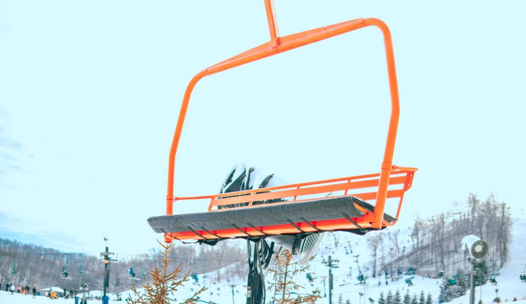 Image showcasing a bustling winter scene at Perfect North Slopes in Indiana, USA. Predominant features include a ski lift carrying skiers uphill, a snowmobile nearby, and multiple skiers enjoying the snowy landscape.