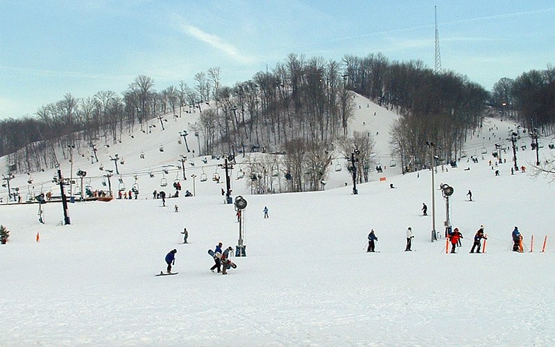 Winter sports enthusiasts enjoying a day at Perfect North Slopes ski resort in Lawrenceburg, Indiana, with stunning winter scenery and ski lifts in the background.