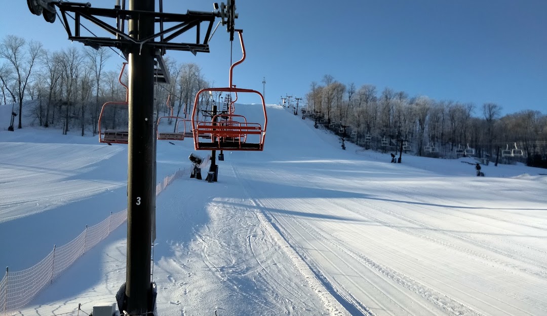A vibrant winter scene at Perfect North Slopes in Indiana with skiers enjoying the snow-covered slopes. A ski lift can be seen carrying skiers to the top of the mountain while a chalet nestles nearby.