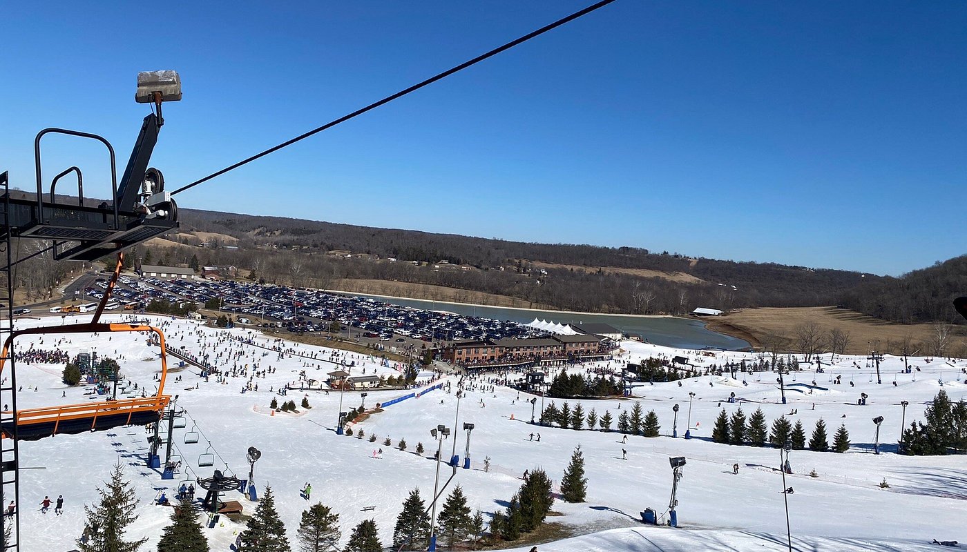 Winter sports enthusiasts enjoy their day at Perfect North Slopes in Lawrenceburg, Indiana. A ski resort filled with skiers on snow-covered slopes and the view of a ski lift and chalet in the distance.