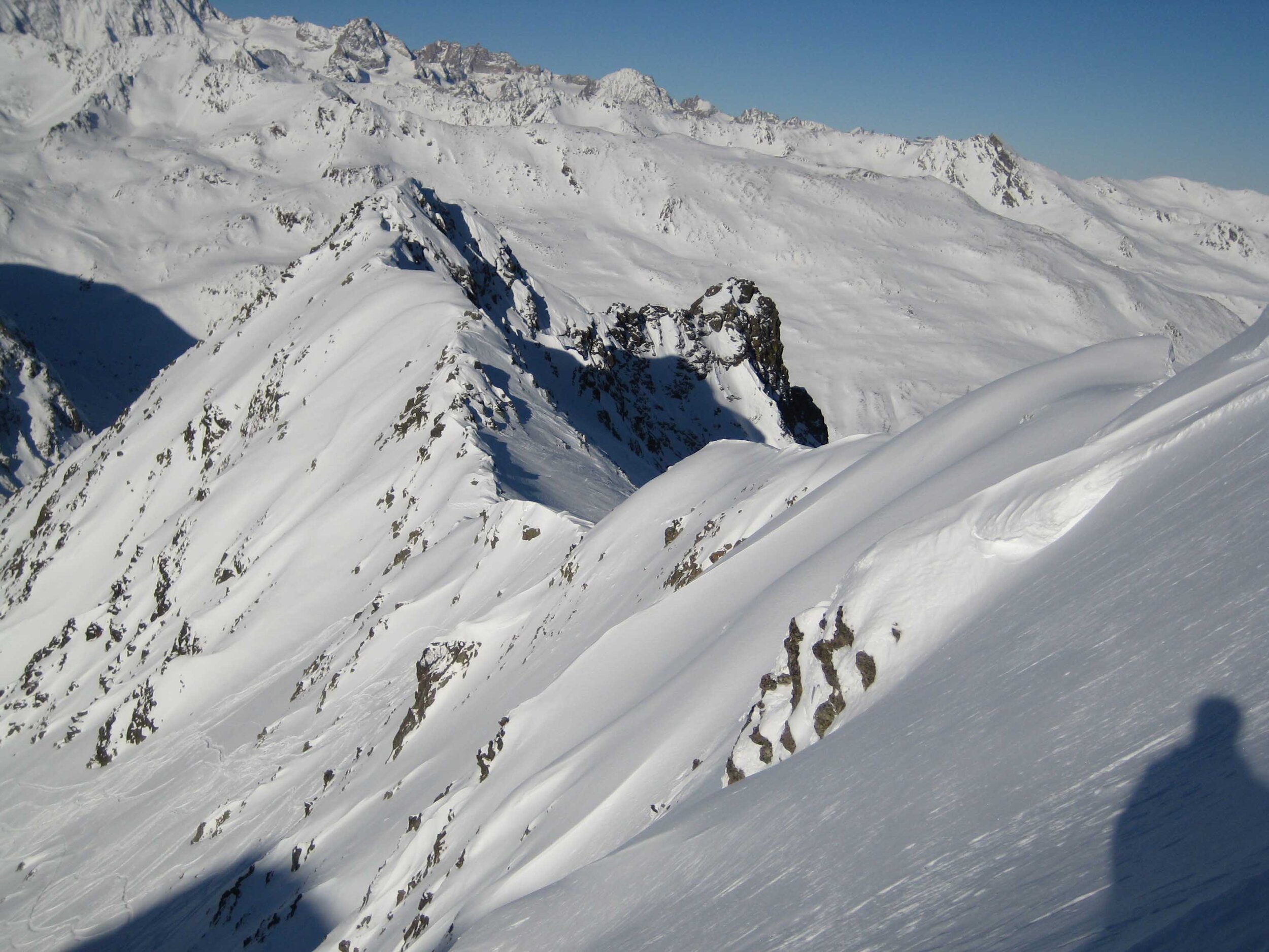 A ski chalet nestled against a mountain backdrop in the snowy landscape of Ruine Super Saint-Bernard, Bourg-Saint-Pierre, Switzerland, featuring solitary skier carving down the slopes.