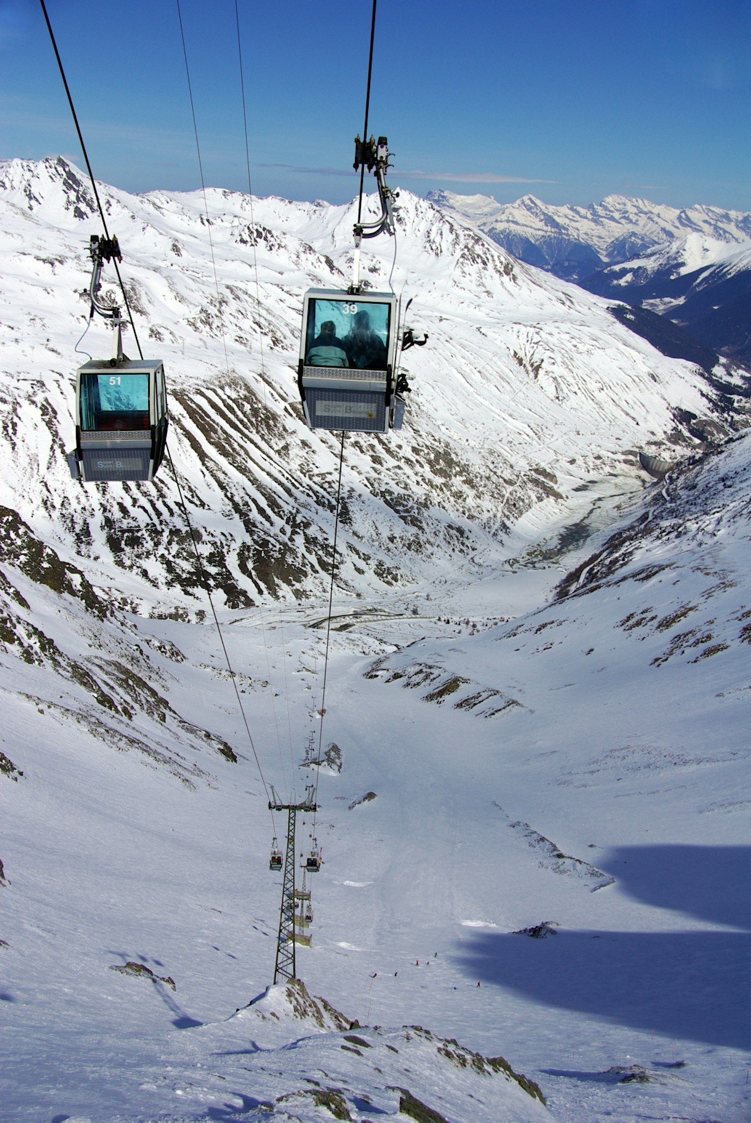 A Swiss winter scene featuring a ski lift near a chalet at Ruine Super Saint-Bernard amid snow-covered ski slopes. The serene ambience typifies a typical Alpine ski resort.