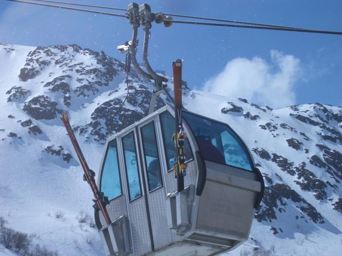 A dynamic scene at Ruine Super Saint-Bernard ski resort in Switzerland featuring a ski lift sweeping across the frame a quaint challet in distance and a skier tackling the slopes.