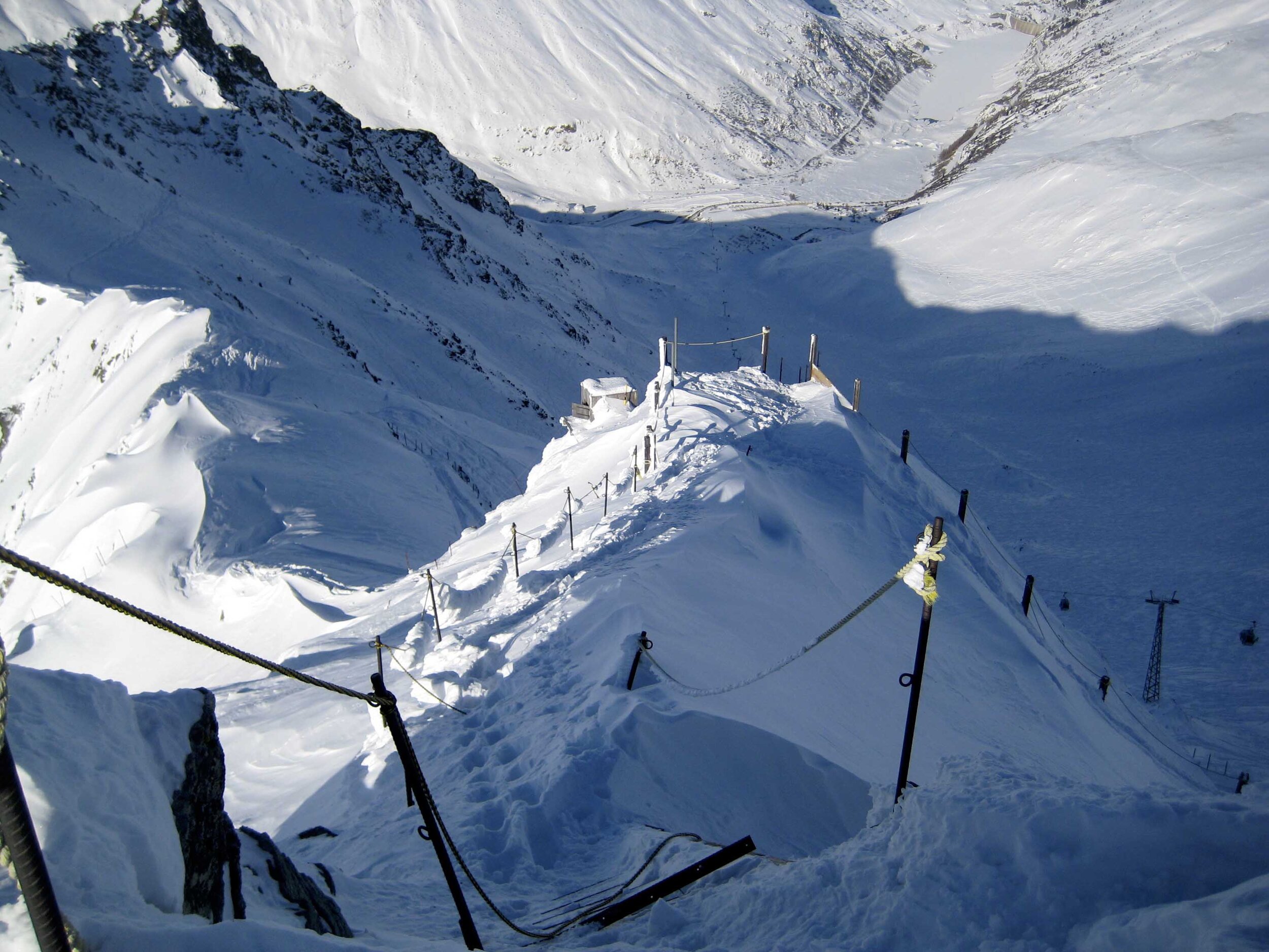 View of the snowy Ruine Super Saint-Bernard in Switzerland, featuring a charming chalet, functioning ski lift, and bustling winter sports centre at a ski resort.