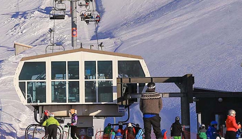 View of Skálafell ski resort in Iceland featuring a ski lift transporting skiers up a snow-covered mountainside, with a cozy chalet nearby.