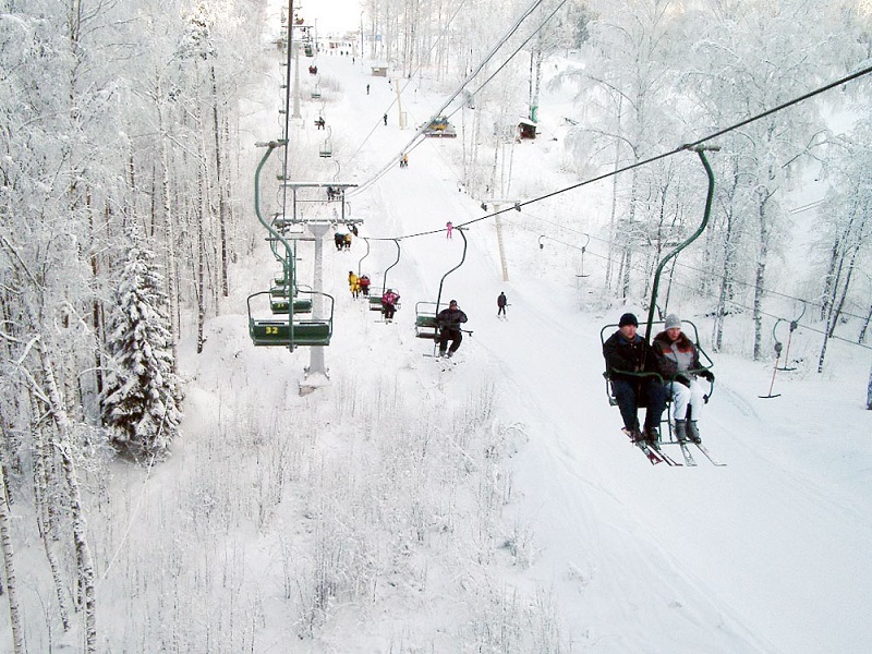 A scenic view of Krasnoye Ozero in Russia featuring a busy ski resort with a ski lift operating, numerous skiers enjoying the winter sport amidst a stunning winter landscape.