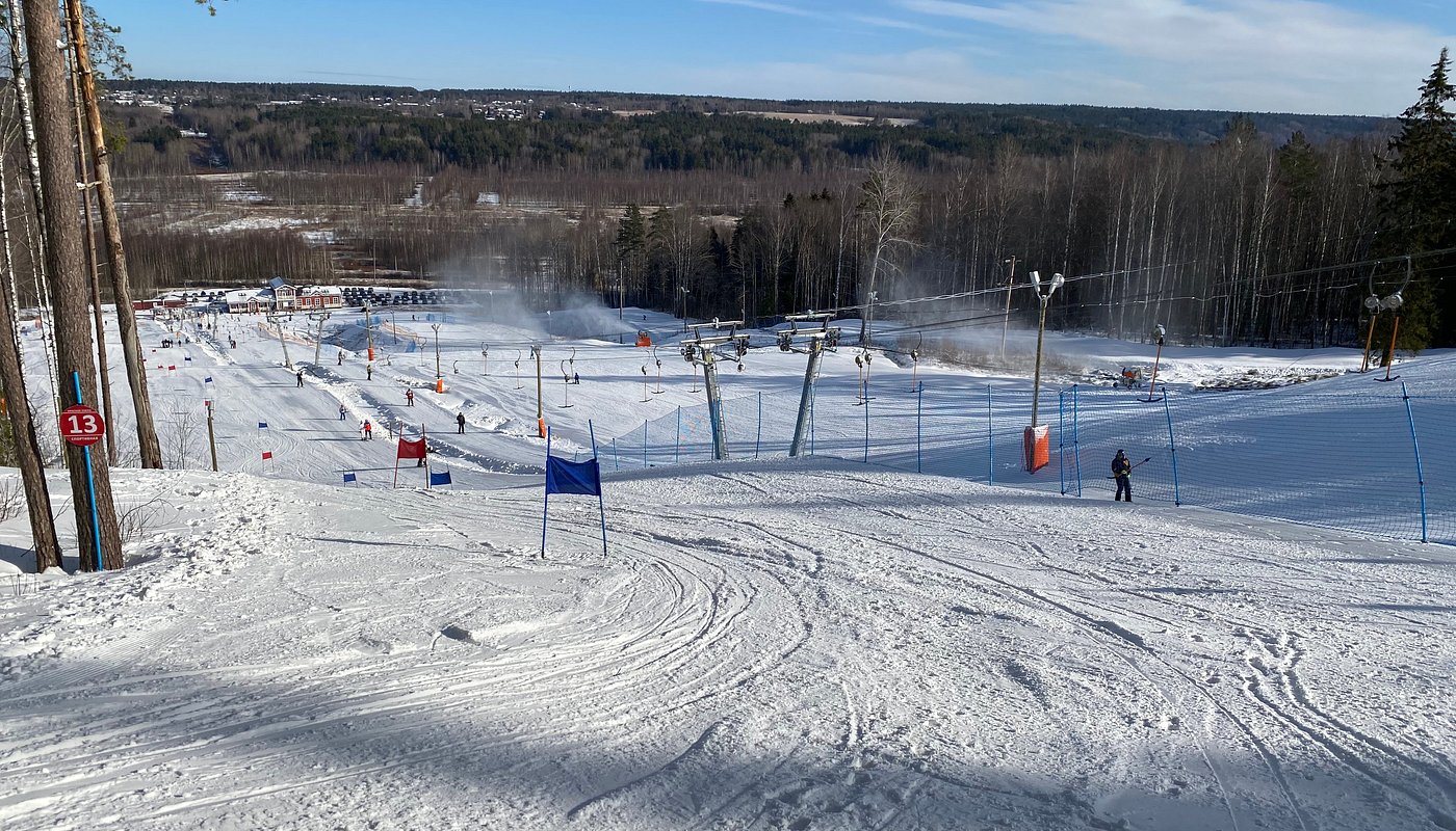 Winter sports enthusiasts in action at Krasnoye Ozero ski resort, Northwest Russia. Ski lift seen imperfectly amidst mountainous backdrop covered in pristine snow.