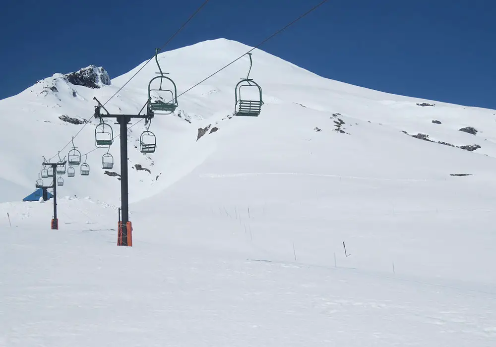 A picturesque view of Vulcan Pass ski resort in Romania featuring a ski lift and a charming chalet nestled among snow-covered slopes with a lone skier adding to the winter wonderland ambiance.
