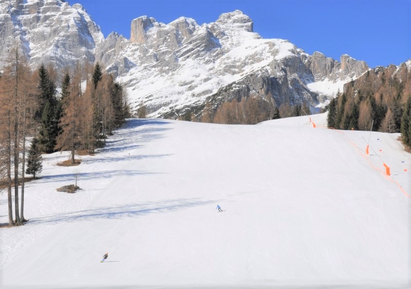 Winter sports scene at Civetta – Alleghe in Belluno, Italy, including a mountain backdrop, a rustic chalet, active skiers, and the bustling ski resort.