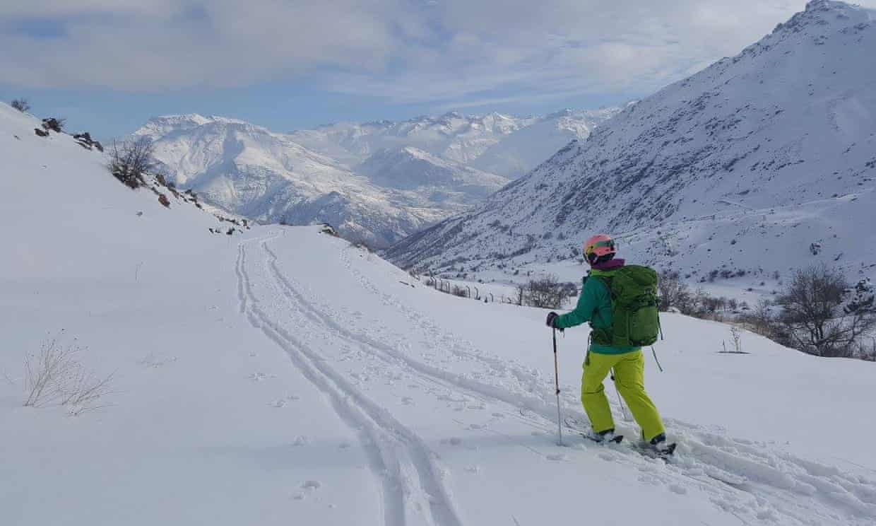 A skier gliding down a snowy slope in Dohuk, Khalifan, Iraq, with a chalet and the garnishing of a winter sports center, all set in a bustling ski resort.