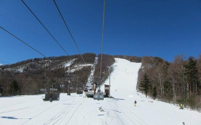 Winter scene at Chateraise Ski Valley Koumi in Japan, featuring a bustling ski resort with a ski lift, a charming chalet, and skiers enjoying the snowy slopes.
