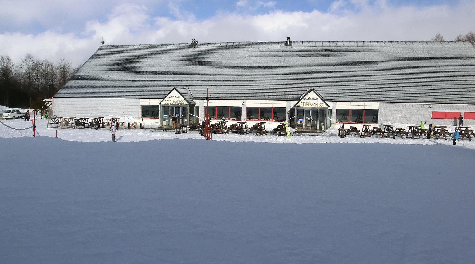 A winter sports scene at Chateraise Ski Valley Koumi, Japan, featuring a bustling winter sports centre and a panoramic view of a ski resort amidst breathtaking winter scenery.