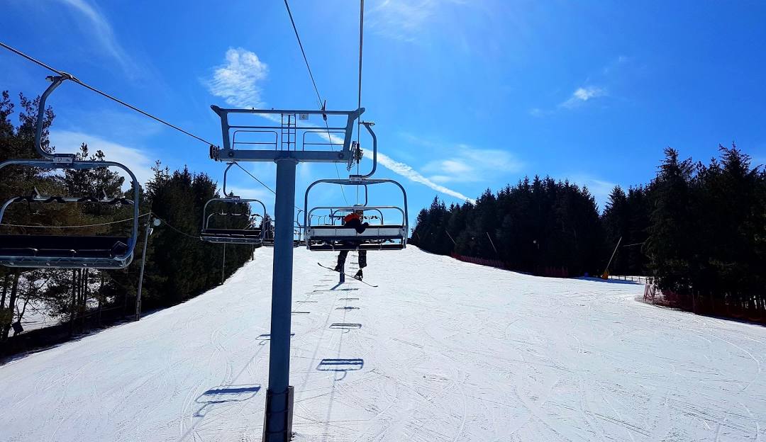 Winter sports scene at Brimacombe ski resort in Orono, Ontario with a ski lift and skier in action, with a chalet in the backdrop.