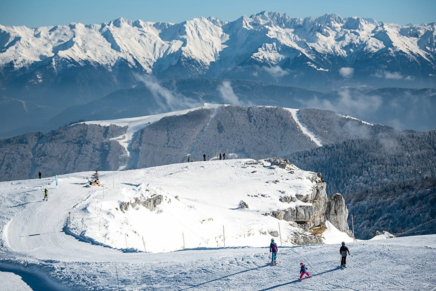 Winter sports enthusiasts gather at a ski resort in Aillon-le-Jeune, France. Snow-covered peaks, chalets dot the landscape while skiers carve their way down the slopes.