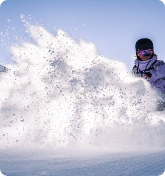 A lively winter sports scene at Peyragudes in France featuring a skier and a snowboarder navigating the snowy slopes. A snowmobile is also visible with a chalet nearby showcasing the quintessential alpine adventures in Hautes-Pyrénées.