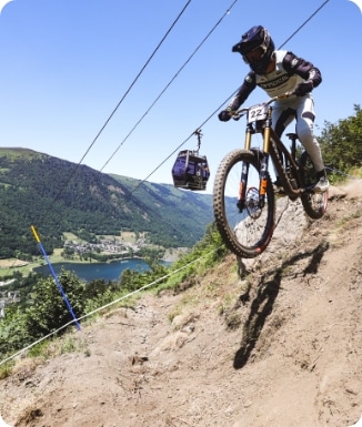 A mountain biker enjoys a ride in the beautiful terrain of Peyragudes in Hautes-Pyrénées France with a quaint chalet visible in the backdrop.