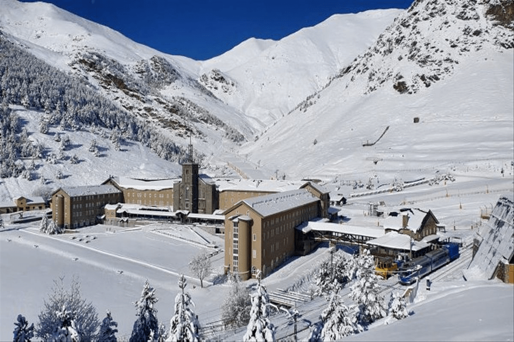 Vall de Núria in Spain: a snow covered mountain with a building in the middle.